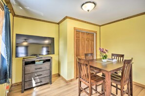 A dining area with a wooden table and chairs, a television mounted on the wall, and a wooden cabinet with drawers.