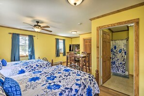 A room with two beds, a ceiling fan, a dining table with chairs, and a bathroom with a shower curtain.