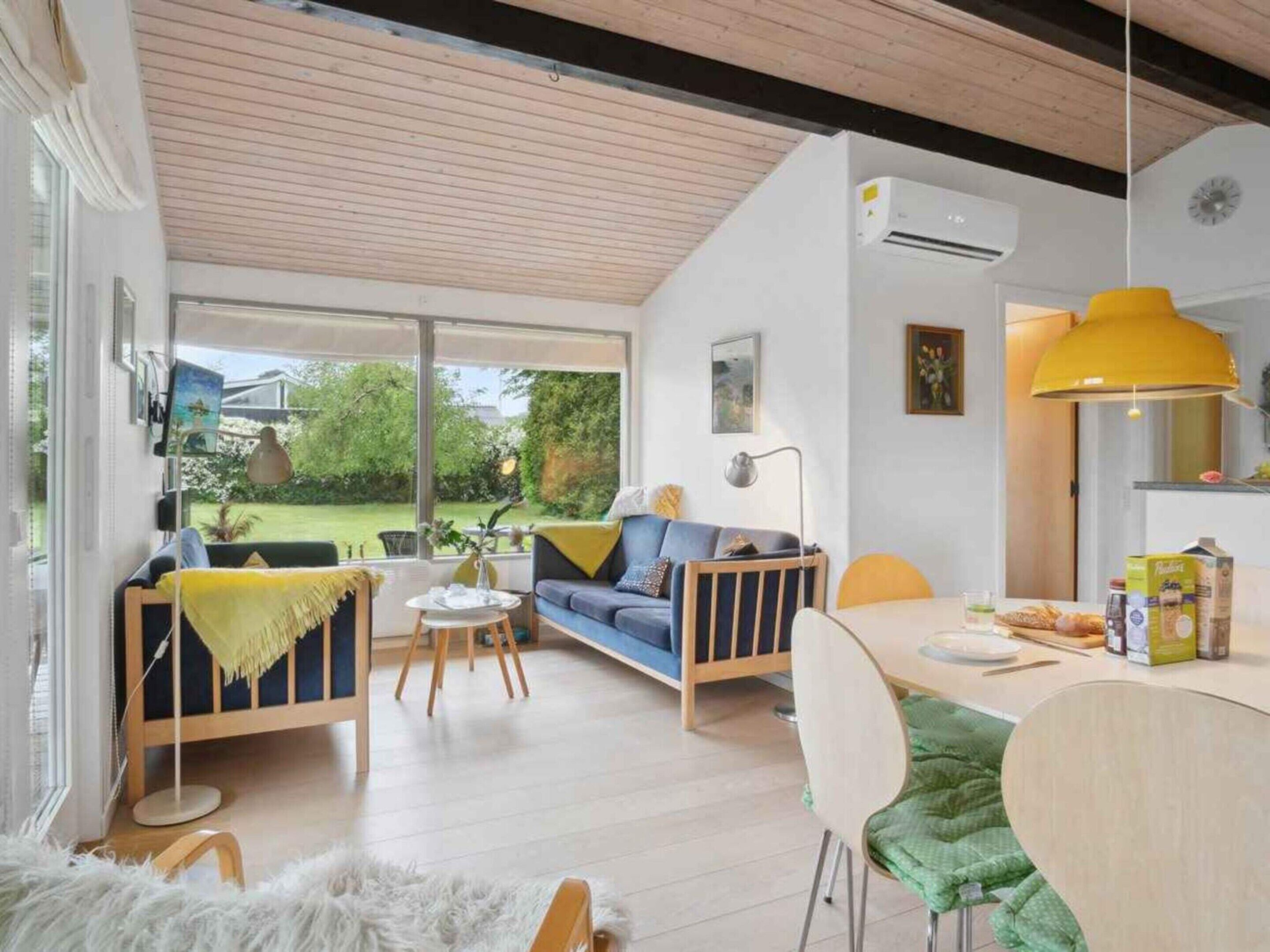 Una sala de estar moderna con un sofá, una mesa de comedor y una zona de cocina con una lámpara amarilla.