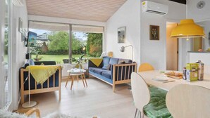 A modern living room with a sofa, a dining table, and a kitchen area with a yellow lamp.
