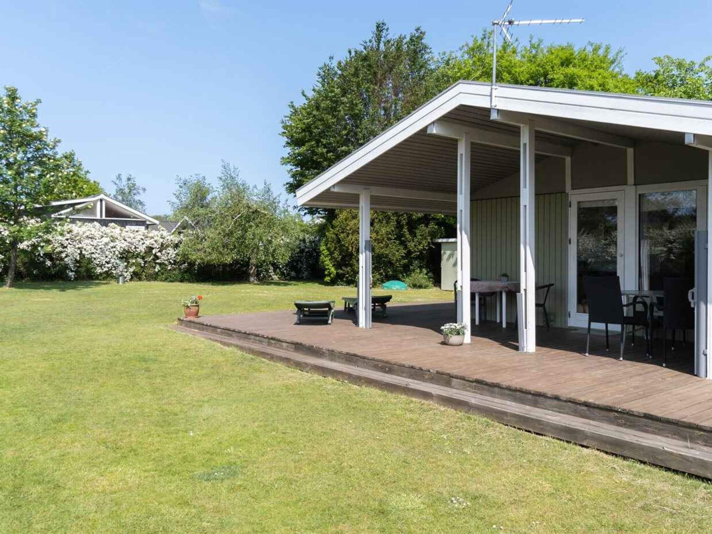 Un patio techado con mobiliario exterior, un pequeño jardín y una casa al fondo.