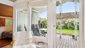 A cozy room with a white furry chair, a small table, and a window overlooking a wooden deck and garden.