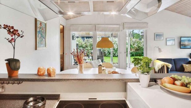 A modern kitchen with a central island, a dining area with a sofa, and a view of the garden through large windows.
