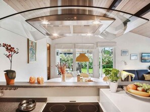 Une cuisine moderne dotée d’un îlot central, d’un coin repas avec un canapé et d’une vue sur le jardin grâce à de grandes fenêtres.