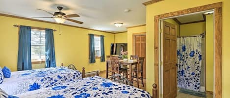 A bedroom with two beds, a ceiling fan, a TV, and a dining area with chairs and a table.