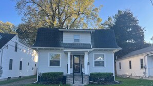 A two-story house with a front porch, a black roof, and a number '1021' on the front door. - Quiet 3 Bedroom home Near downtown (Lansing)