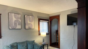 A living room with a grey sofa, a round coffee table, and two abstract wall art pieces. - Quiet 3 Bedroom home Near downtown (Lansing)