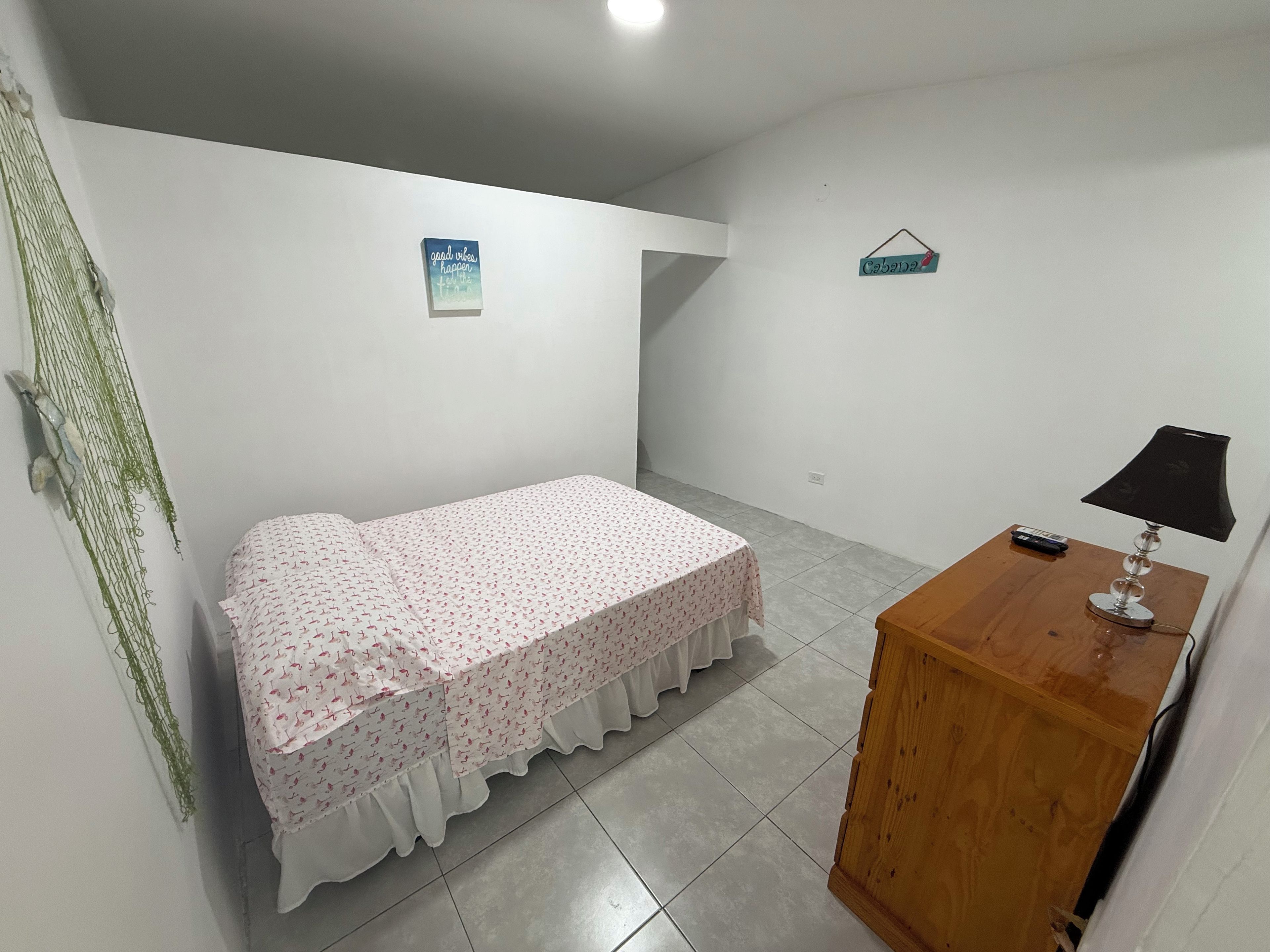 A bedroom with a single bed, a wooden nightstand with a lamp, and a wall-mounted shelf.