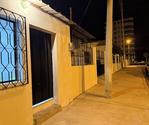 A nighttime street view with a building featuring a barred window and a door, a sidewalk, and a streetlight. - Walking from Chipipe beach studio for 4with AC in charming Salinas (Salinas)