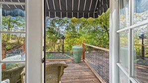 Una terraza de madera con una silla de mimbre, un jarrón verde grande y una valla metálica.