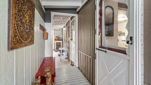 Un pasillo estrecho con un banco de madera, un panel decorativo en la pared y una puerta con espejo.