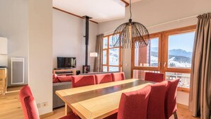 A modern dining room with a wooden table and red upholstered chairs, a television, and a view of a snowy landscape through large windows. - Monarchs 703 (Bourg-Saint-Maurice)