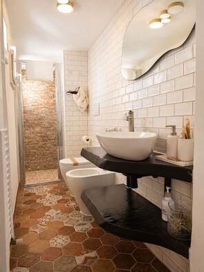 A modern bathroom with a stone shower, white tiled walls, a large mirror, and a black countertop. - Byzantine Villa (Ravenna)