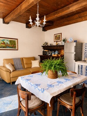 A cozy living area with a sofa, a dining table with chairs, a chandelier, and a kitchen area with appliances.