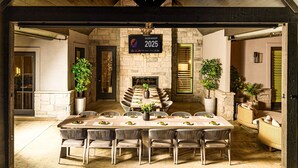 Une longue table à manger, entourée de chaises, de murs en pierre et de poutres en bois, avec une pancarte indiquant qu’un événement de lancement de campagne de vente aura lieu en 2025.
