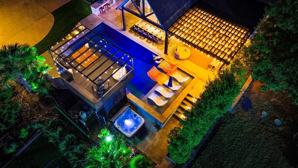 Vue aérienne d’un espace piscine extérieur moderne, comprenant un jacuzzi, des sièges et un patio couvert.