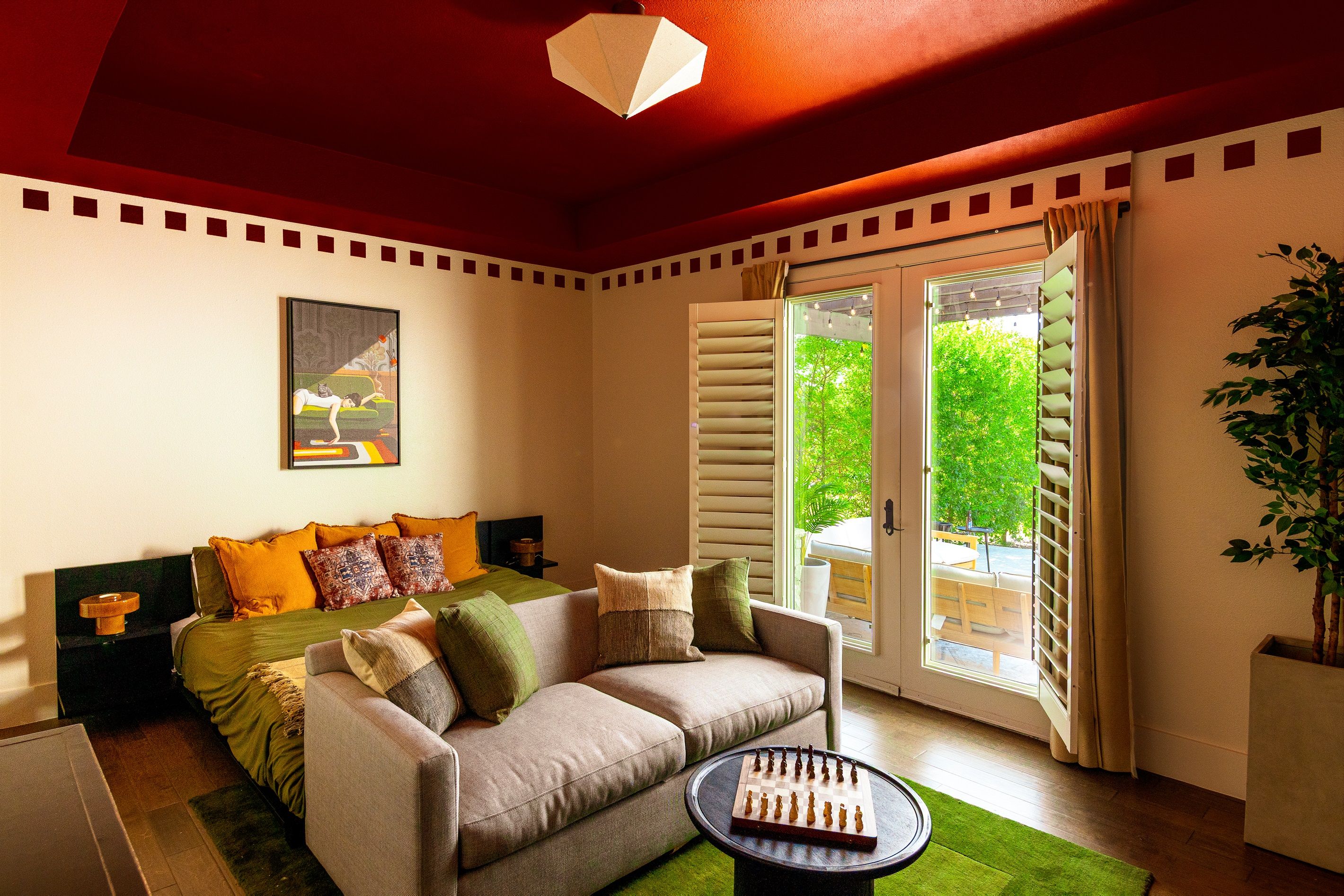 A room with a sofa, a chess table, and a large window with shutters.