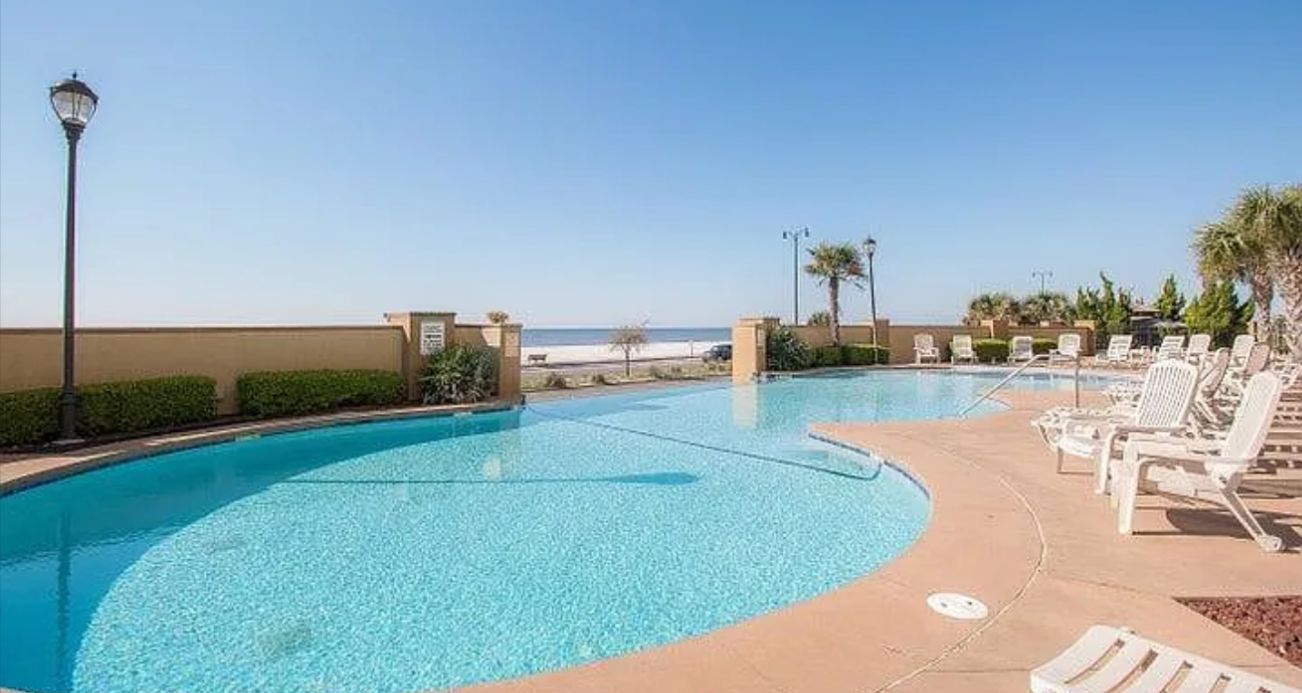 En swimmingpool med liggestole og udsigt til stranden.