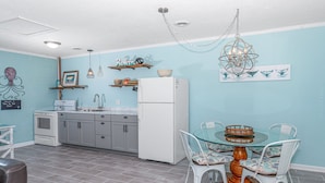 Una cocina con un refrigerador blanco, una estufa y un lavamanos. Hay una mesa de comedor con sillas y una araña colgante arriba.