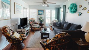 Ein Wohnzimmer mit einer Couch, zwei Sesseln, einem Couchtisch, einem Fernseher und einem Deckenventilator.