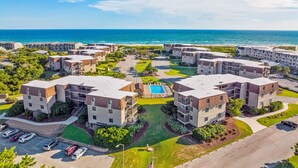 Un complejo residencial con varios edificios de apartamentos, una piscina central y vista al océano.