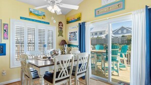 Un coin repas avec une table et des chaises, un ventilateur de plafond et une vue sur le jardin à travers des portes vitrées.