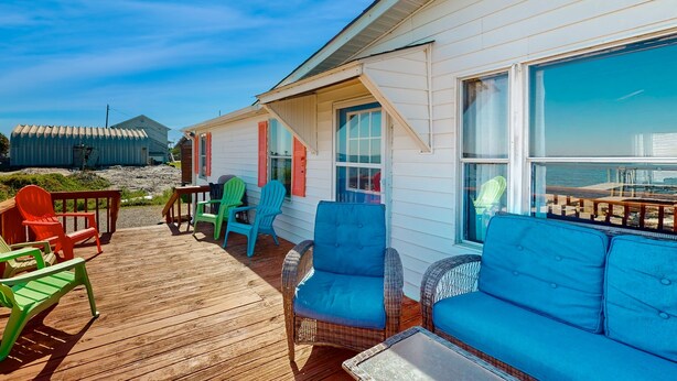 Une terrasse en bois, agrémentée de meubles en osier et de chaises colorées, qui offre une vue sur la plage.