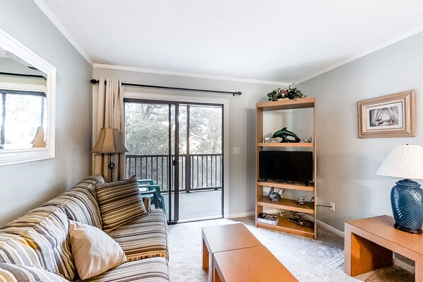 A living room with a sofa, a coffee table, a TV stand, and a sliding glass door leading to a balcony.