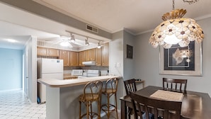 A modern kitchen with wooden cabinets, a white countertop, and a dining area with a table and chairs. - First-Floor Condo in Soundside Complex with WiFi, W/D & Shared Pools/Gym/Tennis (Atlantic Beach)