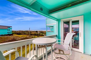 Een balkon met een tafel en stoelen, een deur met ruitpaneel en uitzicht op een gebouw en landschap.