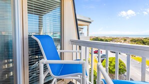 En balkon med en blå stol og udsigt over vejen og grønne områder.