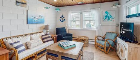 A cozy living room with a wooden ceiling, a sofa with cushions, a table, a television, and a window with blinds.