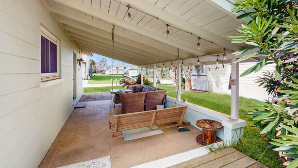 Une terrasse couverte avec une balançoire en bois, du mobilier d’extérieur et une petite table.