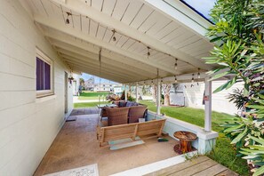 Une terrasse couverte avec une balançoire en bois, du mobilier d’extérieur et une petite table.