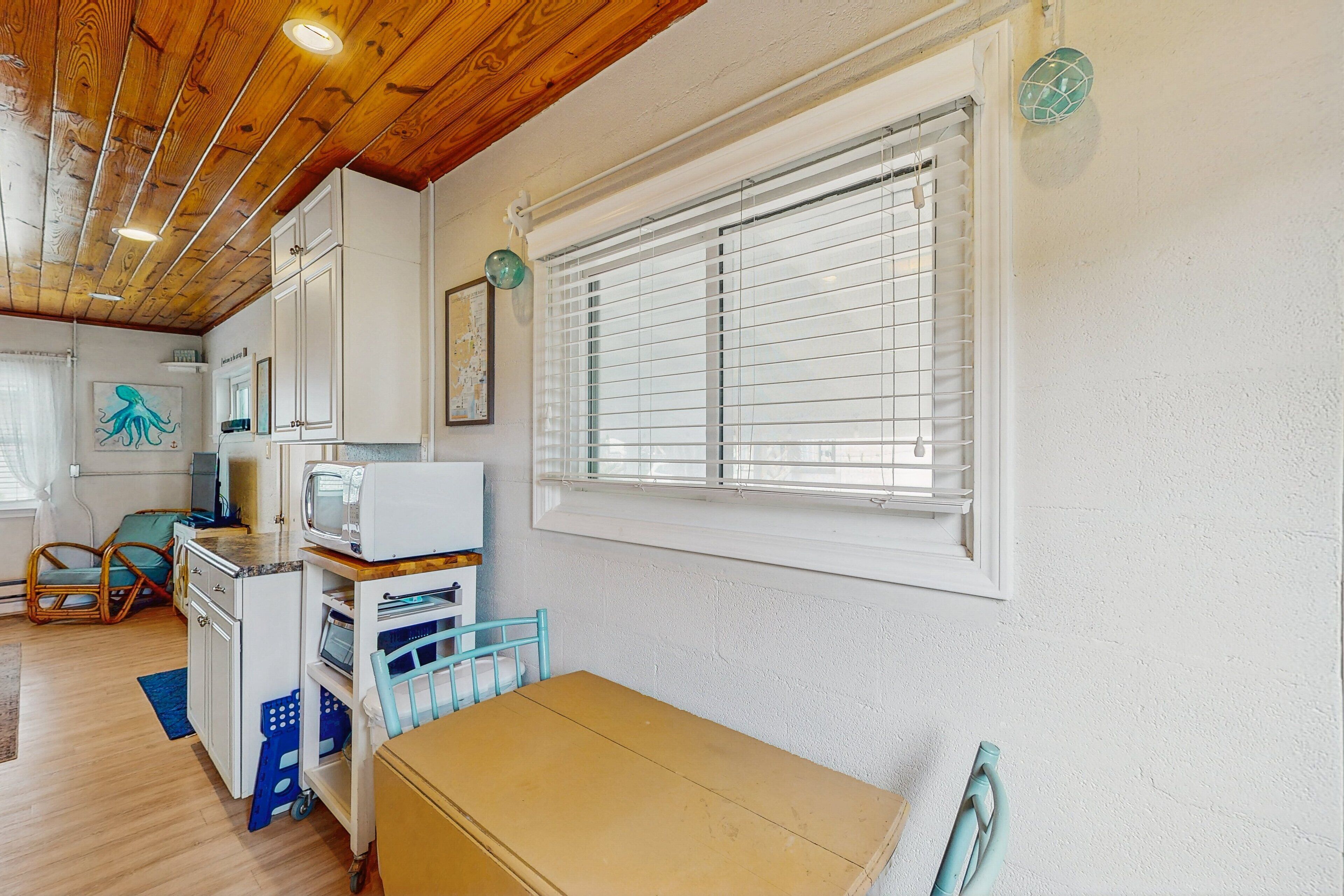 A room with a wooden ceiling, white walls, a window with blinds, a desk with a computer, and a chair.