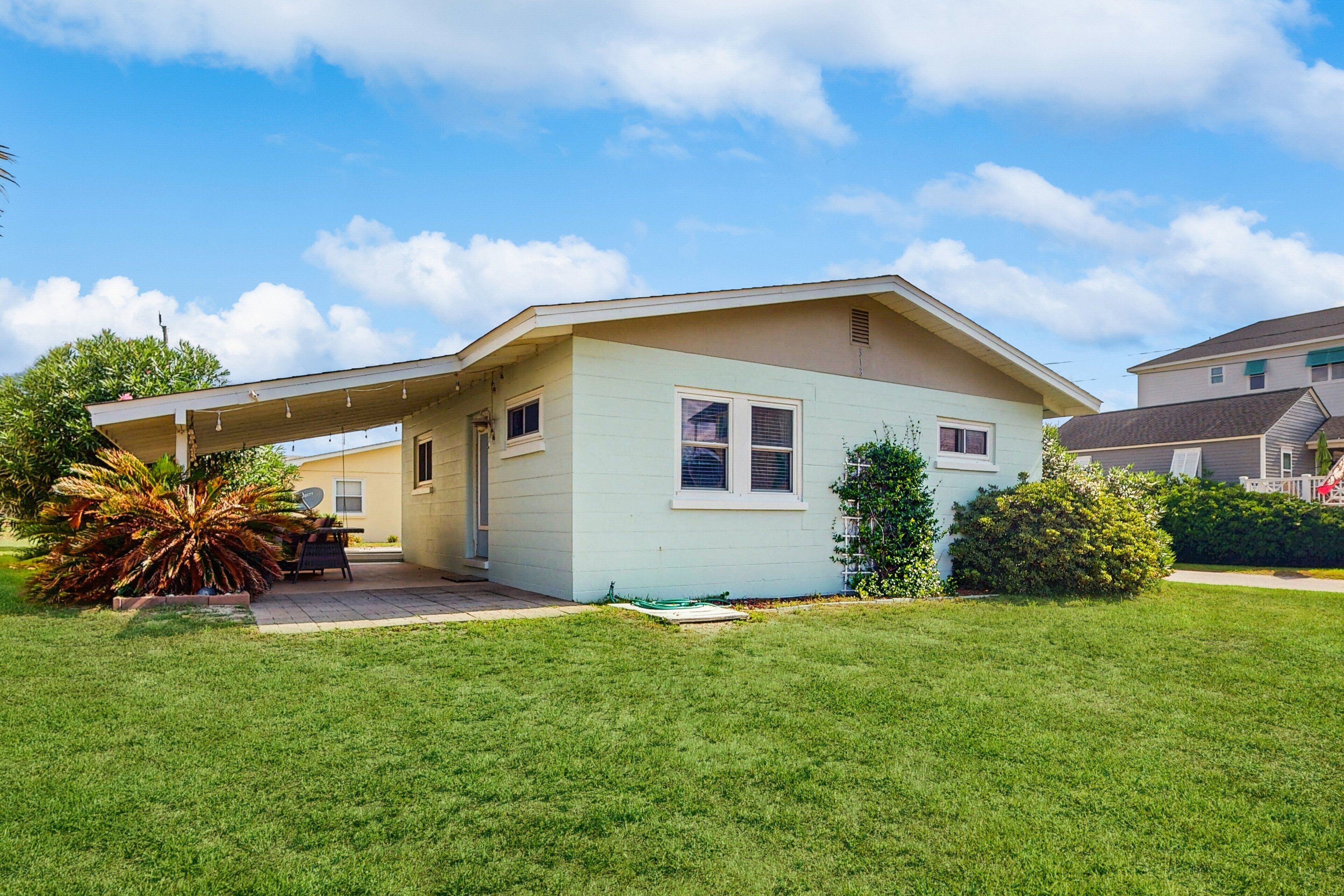 A single-story house with a covered patio, a lawn, and a small garden.