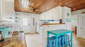 Une cuisine avec des meubles blancs, une table de couleur turquoise et des tabourets de bar bleus.