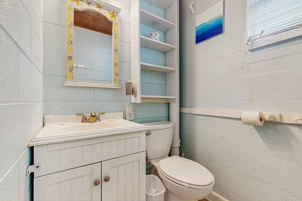 Une salle de bain avec un meuble-lavabo blanc, des toilettes et une étagère avec des boîtes de rangement.