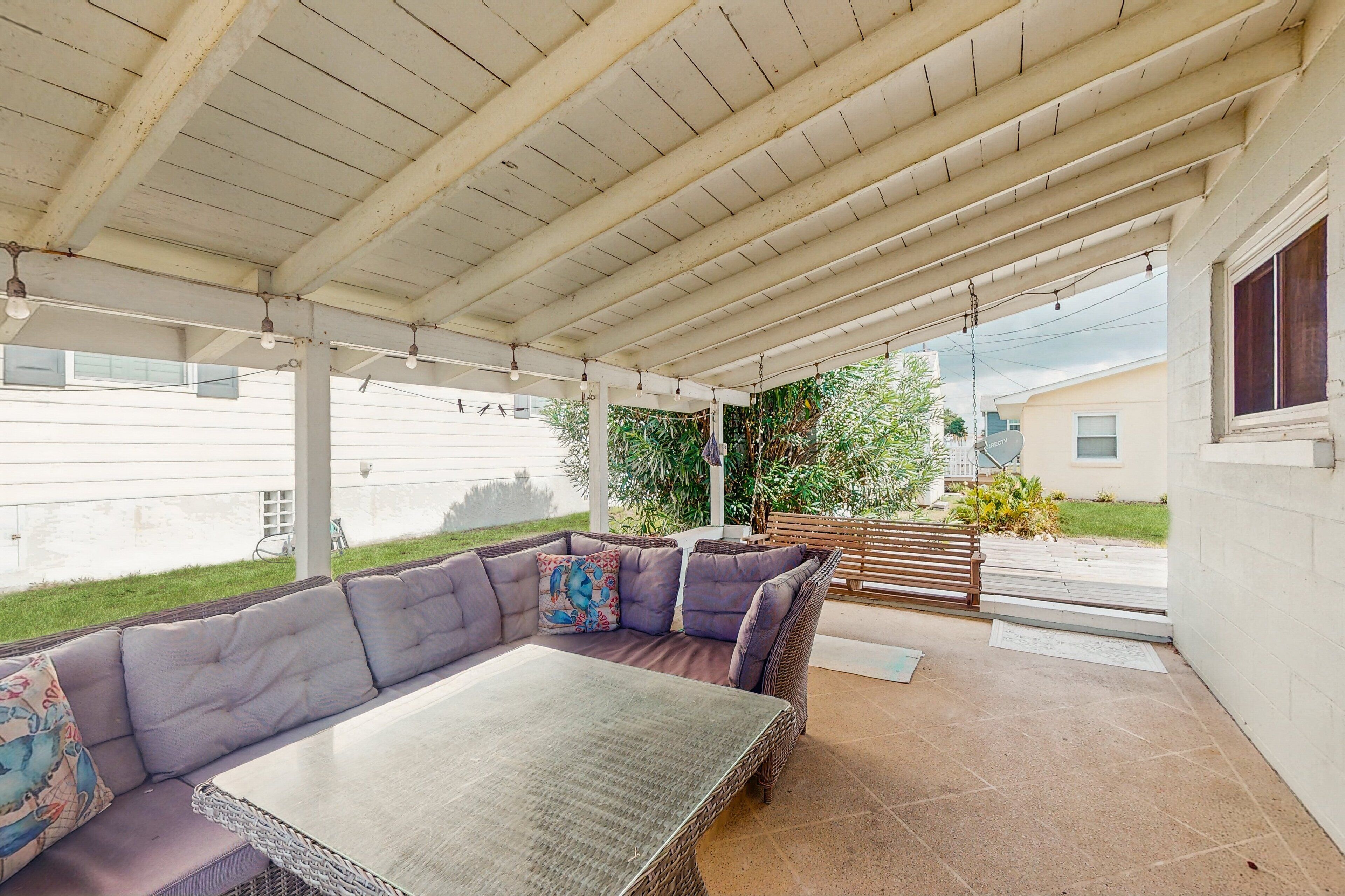A covered patio area with a cushioned seating arrangement and a table.