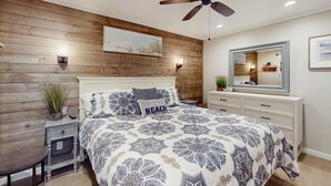 A bedroom with a wooden wall panel, a ceiling fan, a bed with a patterned bedspread, a nightstand, a chair, and a dresser with a mirror. - Wonderful Third-Floor Condo in Oceanfront Complex w/Shared Pools & Hot Tub, WiFi (Atlantic Beach)