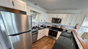 Una cocina moderna con electrodomésticos de acero inoxidable, armarios blancos y encimera negra.