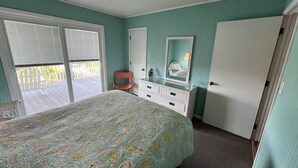 Un dormitorio con cama, cómoda, una silla y puerta corrediza de vidrio que da a un balcón.