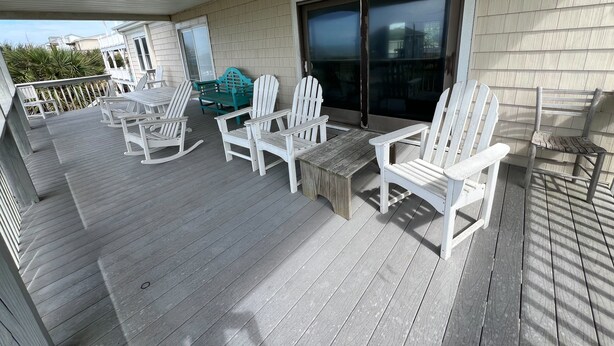Una terraza techada al aire libre con sillas Adirondack blancas, una silla Adirondack verde y una pequeña mesa.