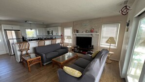 Una sala de estar moderna con un sofá gris, una mesita de centro y un televisor. Se observa una zona de cocina con armarios blancos y un microondas.