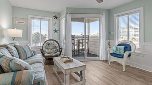 Una habitación con sofá, una silla, una mesita, ventilador de techo y puerta corrediza de vidrio que da a un patio exterior.