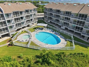 A multi-story hotel with a central swimming pool, outdoor seating, and a view of a lake.