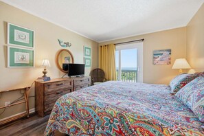Habitación de hotel con cama, televisión, cómoda, silla y balcón con vistas.