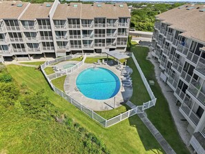 A multi-story hotel with a central swimming pool surrounded by a fence, balconies, and a well-maintained lawn.