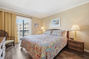 A hotel room with a bed, two bedside lamps, a chair, a dresser, and a balcony with curtains.