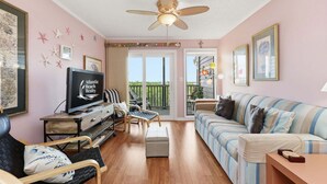 A living room with a ceiling fan, a television, a sofa, a coffee table, and a balcony with a view. - Well-Appointed Condo with WiFi, Washer/Dryer & Shared Pools, Tennis (Atlantic Beach)